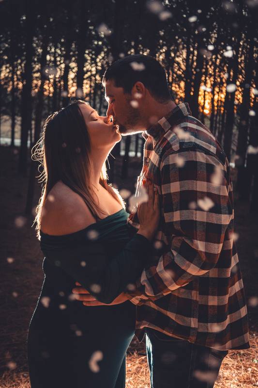 Couple kissing in the woods with light behind them