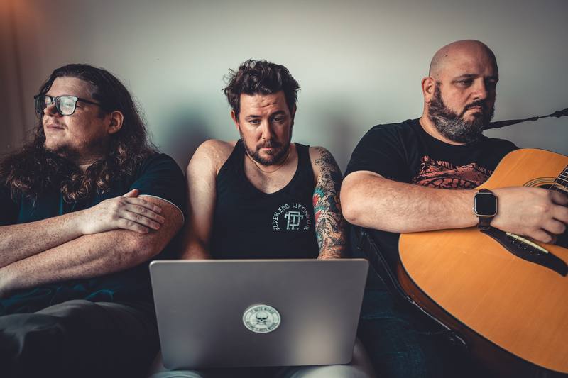 Three band members with a guitar and laptop